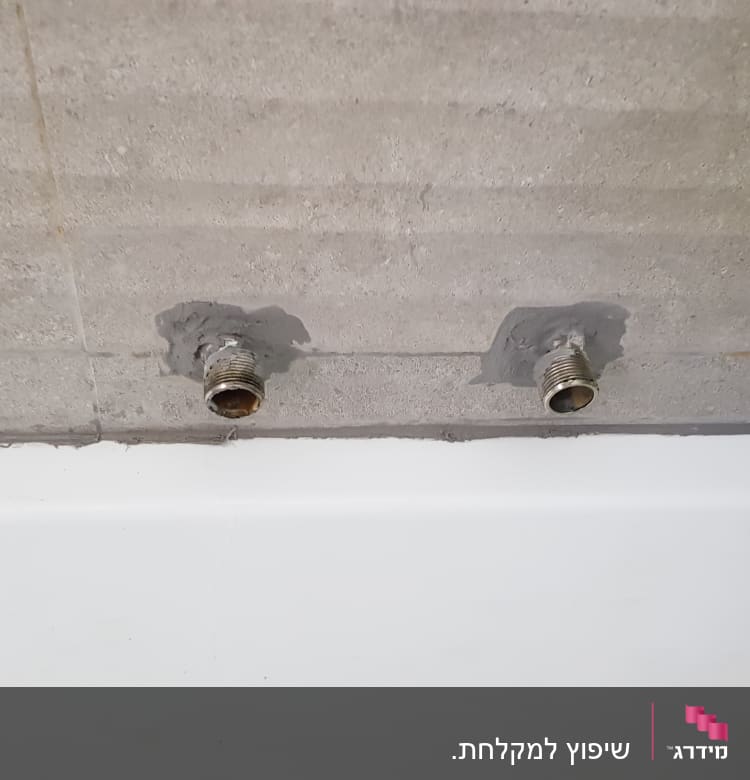 שני צינורות מתכת מותקנים בקיר בטון